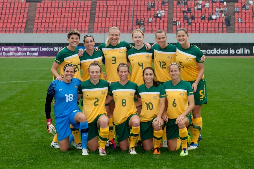 A women's soccer team wearing yellow and green poss for a photo before a game