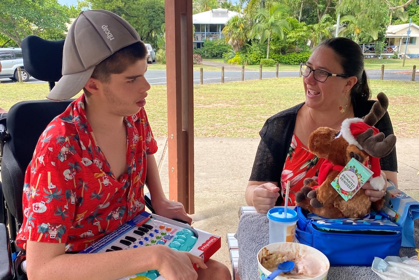 Nic Bennett wears a Christmas shirt and looks at his presents at a park table