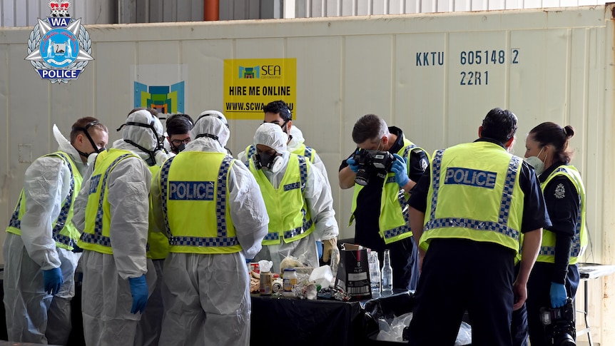 Police in forensic suits sort through rubbish on a table.