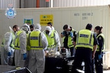 Police in forensic suits sort through rubbish on a table.
