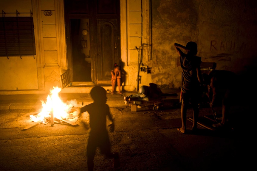 A few people, including children, are gathered near a fire outside a property at night.