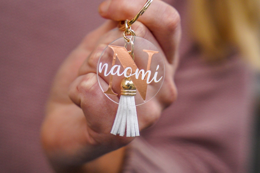 A clear glass circle with the name 'Naomi' printed on in pink, attached to a tassel and key ring.