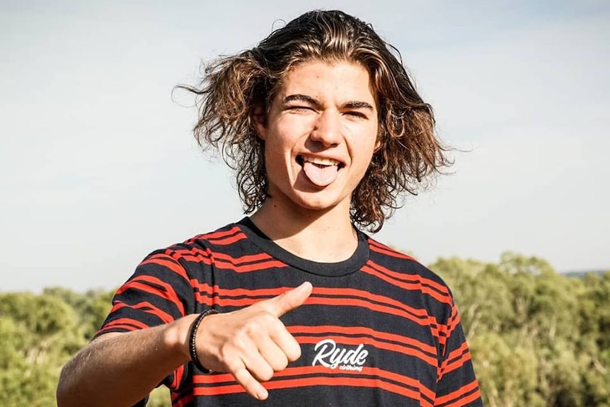 A young man, wearing a red-and-black striped t-shirt, makes a 'hang loose' sign with his hand