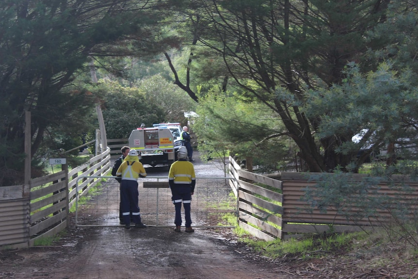 People in high-vis clothes near the gate of a property which is flanked by green trees.