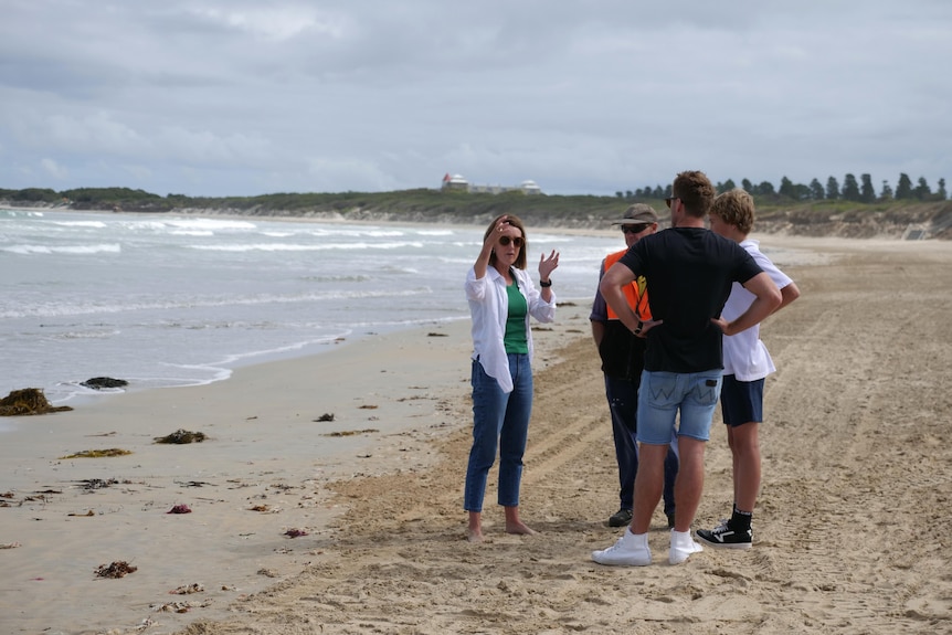 A group of fit healthy people talk on Warrnambool beach with Norfolk pines in distance