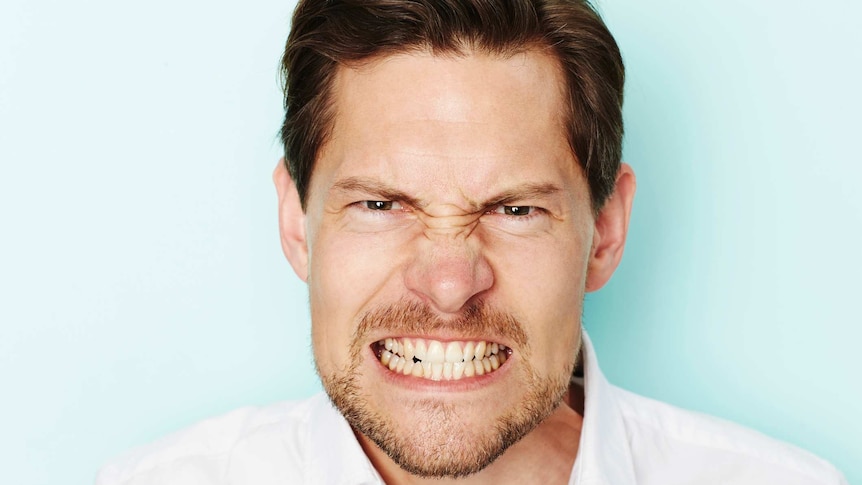 A man clenches his teeth and appears angry, while looking directly at the camera