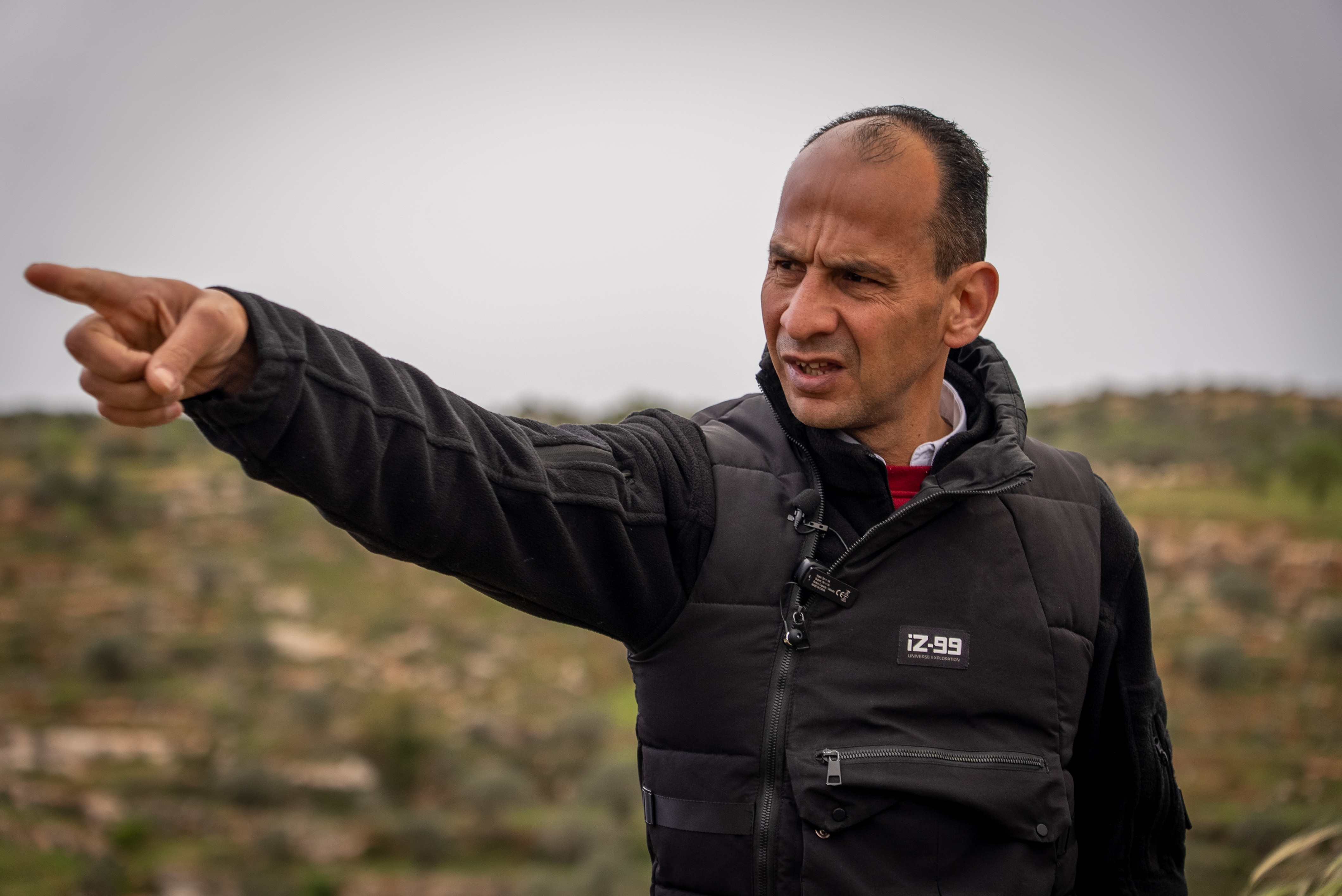 Palestinian Bashar Qaryout dressed in a black jacket points with his hand.