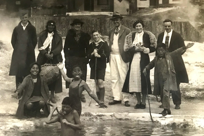 A black and white photo of a group of people standing in front of a natural hot spring in Rotorua, New Zealand.