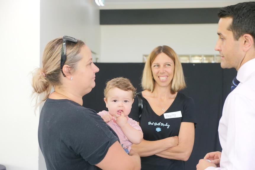 Two women, one holding a baby, speak with a man