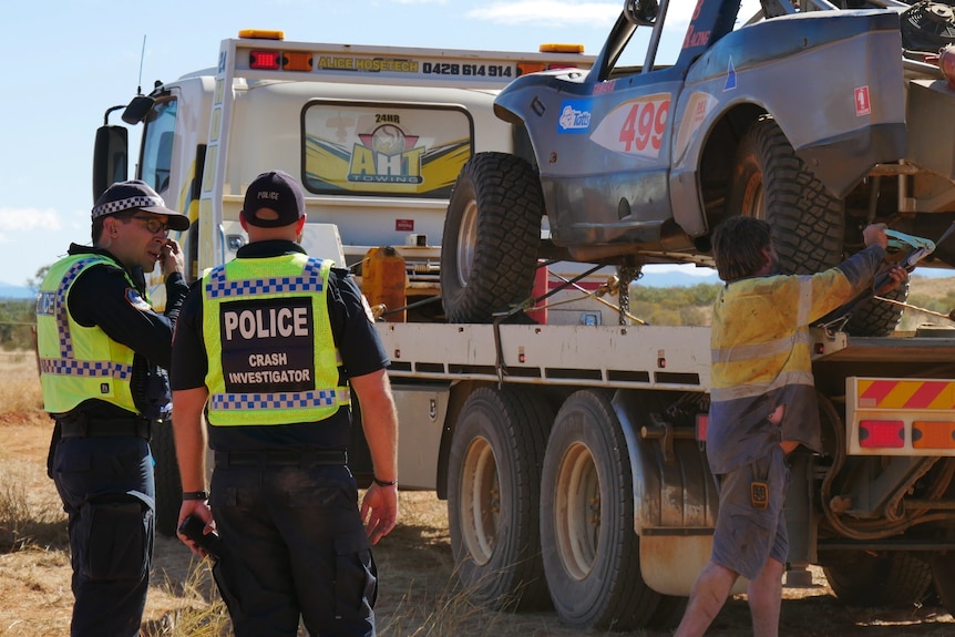 Crash investigators inspect an off-road vehicle which has been loaded onto a truck.