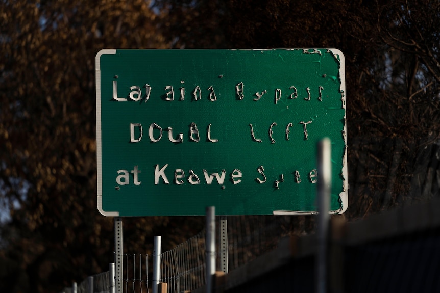 A green road sign with the white letters peeling off