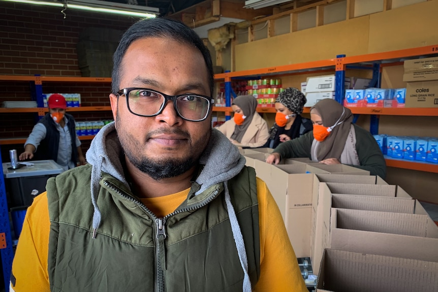 Man with glasses standing behind women packing boxes.