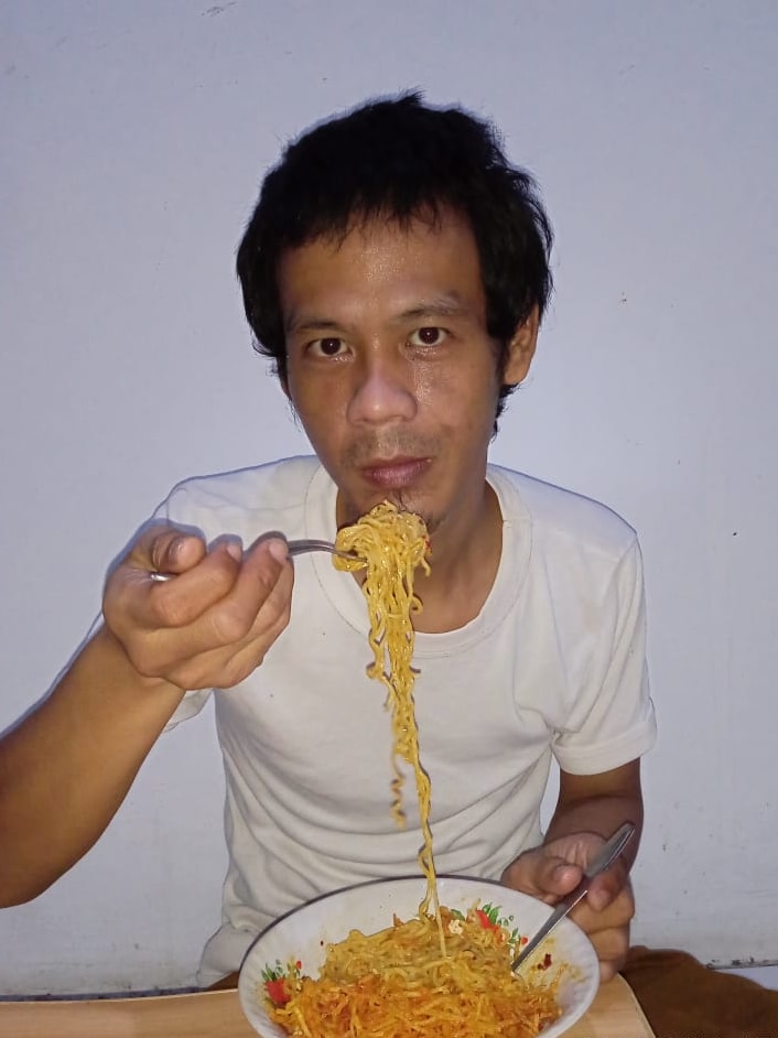 Pria yang melihat ke kamera dan makan mie instan.