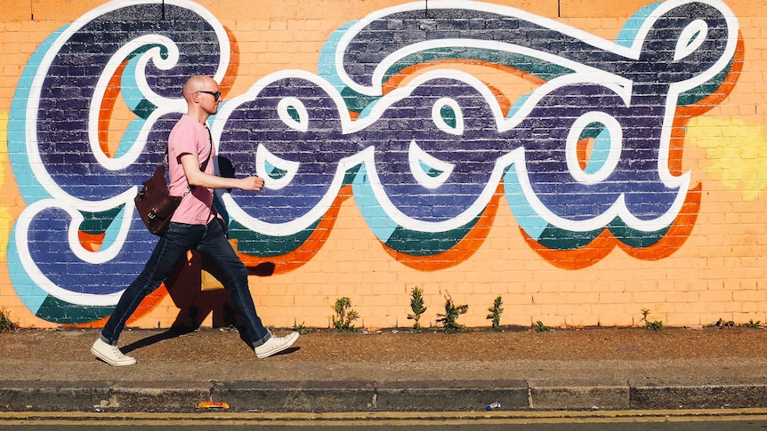 A man walks past a mural with the word "good", depicting a worker interested in building good team culture.