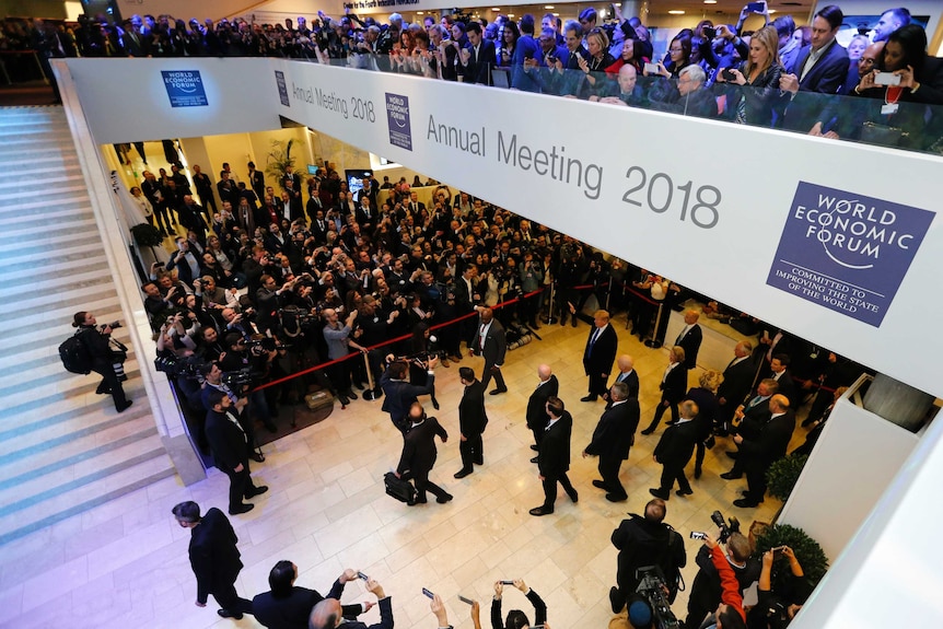 Aerial shot of Donald Trump arriving at the World Economic Forum, with a crowd of people taking photos of him.