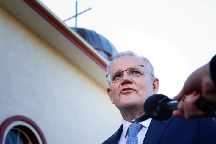 A microphone is given to Scott Morrison who stands in front of a church.