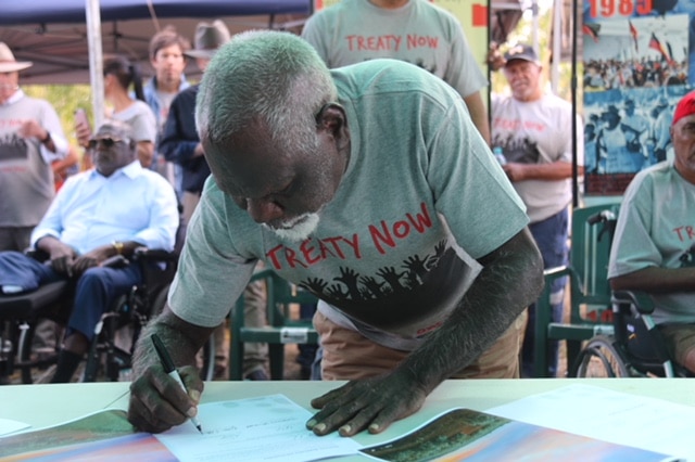 A man wearing a "treaty now" tshirt signs.