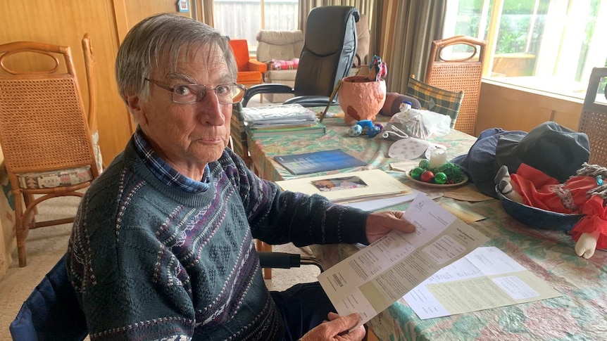 Peter Wood seated at a table holding a piece of paper.