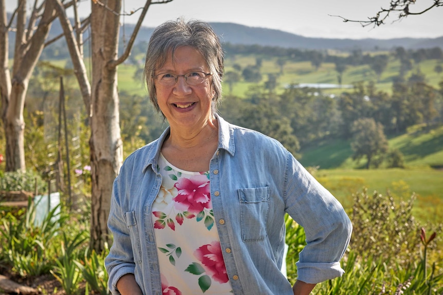 Zena stands in front of a field with trees, smiling at the camera