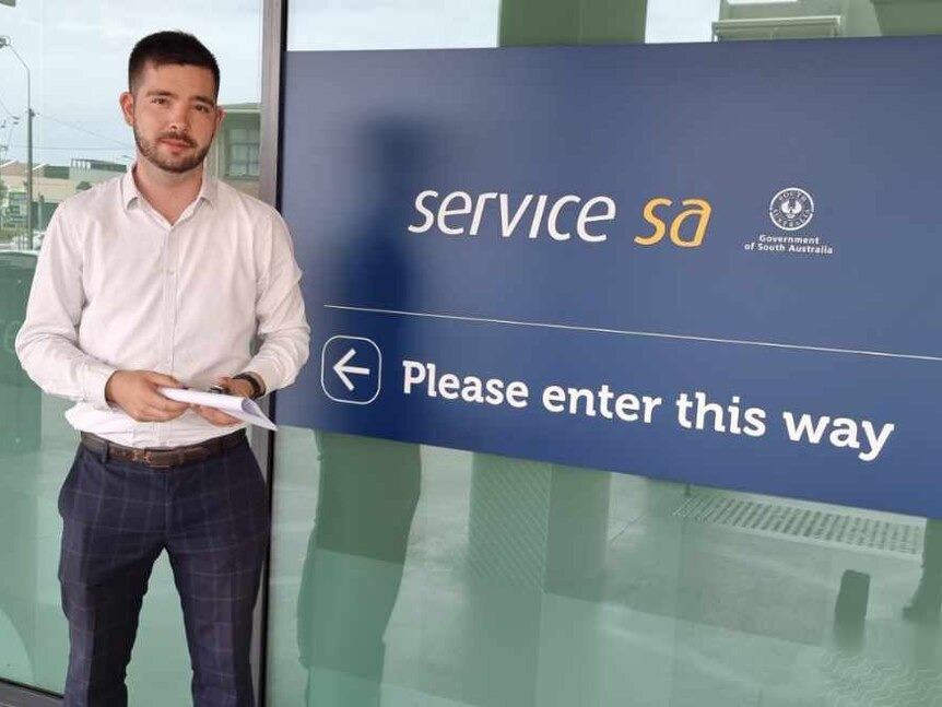 A man standing out the front of a Service SA sign. 