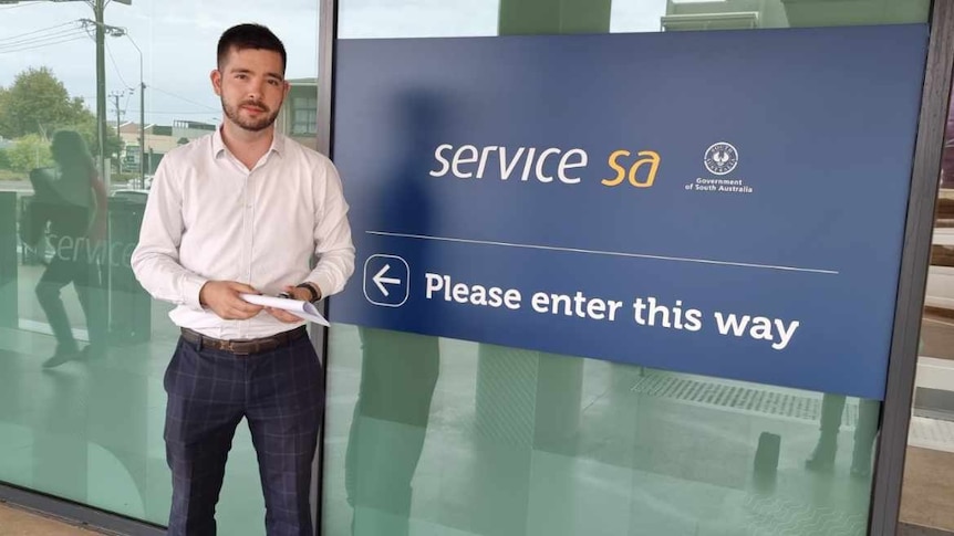 A man standing out the front of a Service SA sign. 