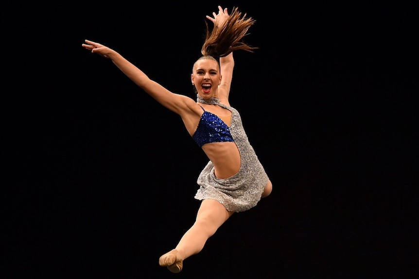 A woman jumps across the stage while dancing.