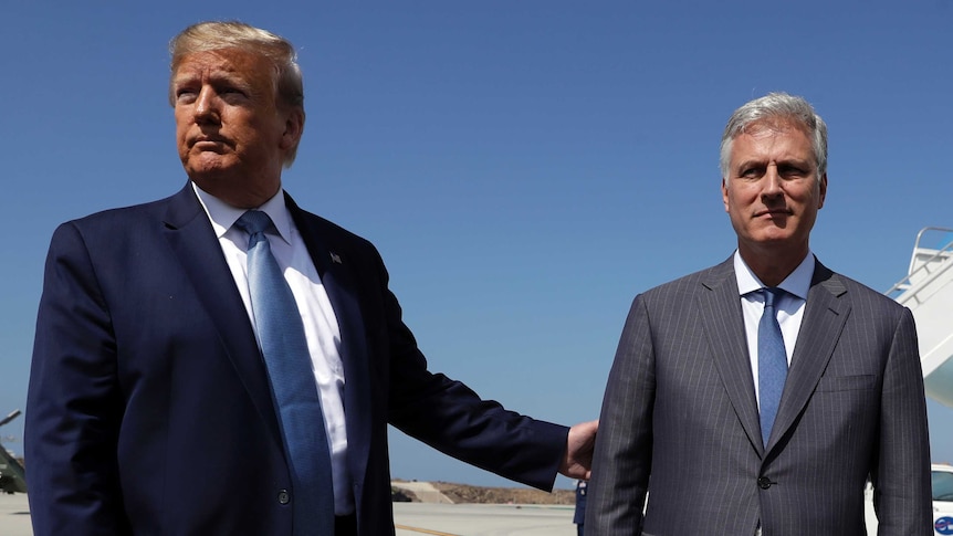President Donald Trump holds the arm of Robert O'Brien as they stand on an airport tarmac.