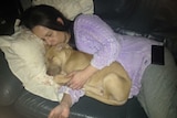A woman lying on the couch hugging a dog.