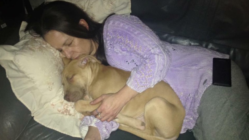 A woman lying on the couch hugging a dog.