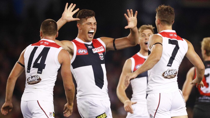 One AFL player grins after a goal while his teammates also celebrate.