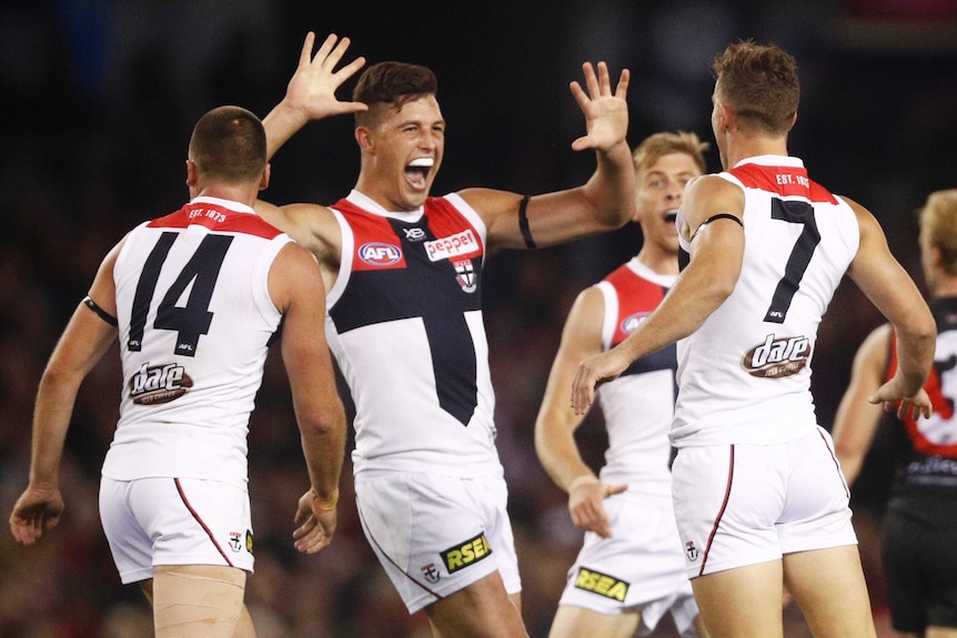 One AFL player grins after a goal while his teammates also celebrate.