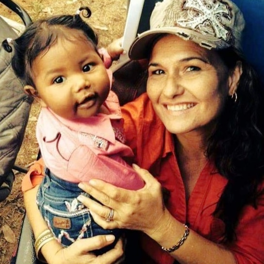 A profile photo of a woman wearing a trucker cap smiling and holding a little girl