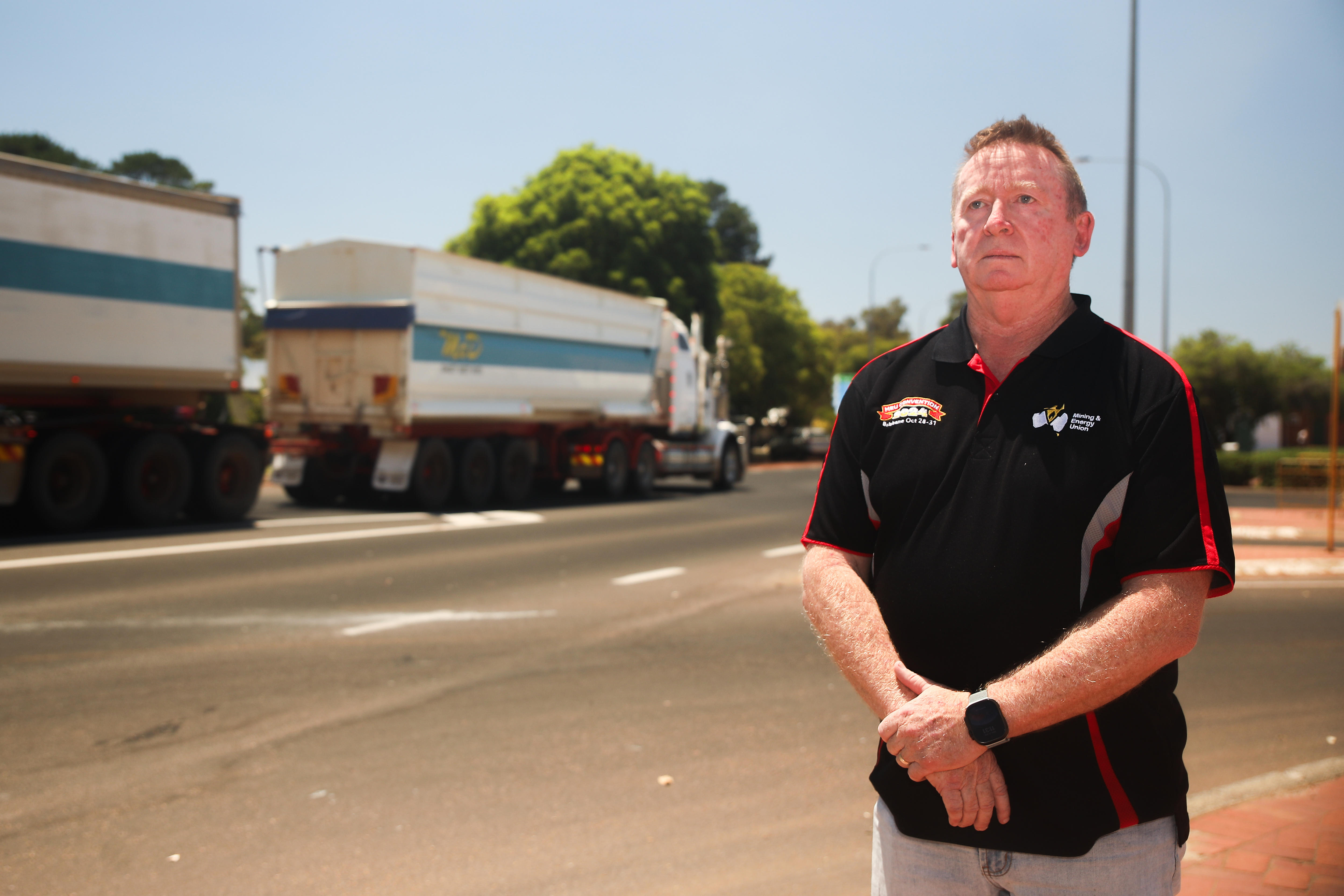 A man stands on the side of the road as a truck passes by