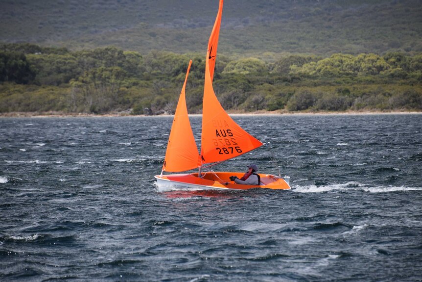 A woman sails in a tiny boat with bright orange sails.