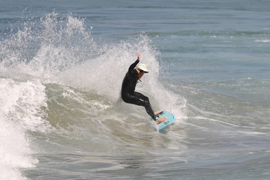 A man in a black surf suit and white hat surfing