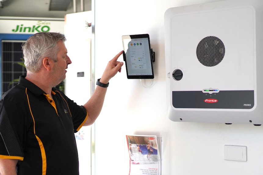 A man presses a wall-mounted screen for a solar energy device.