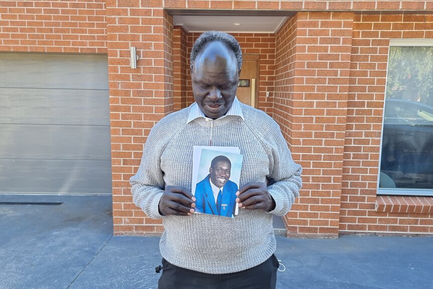 South Sudanese man holding a photo of William Orule.