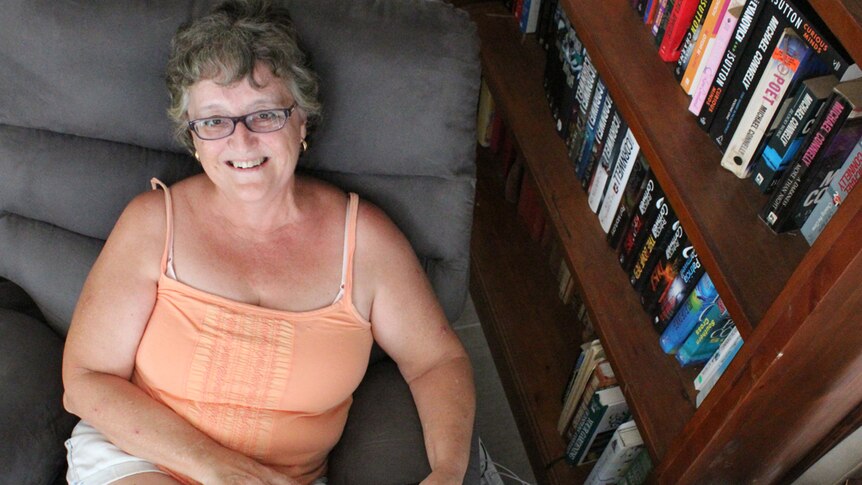 Woman sits in comfy lounge chair with a book on her lap smiling