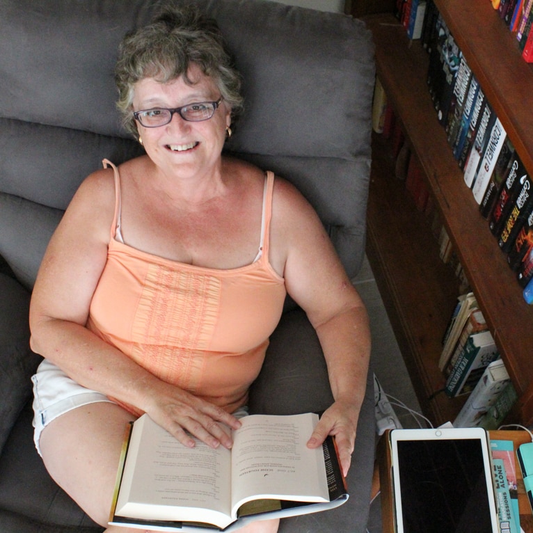 Woman sits in comfy lounge chair with a book on her lap smiling
