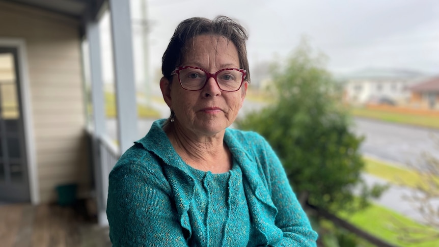 An woman stands on a verandah  with a serious look on her face.