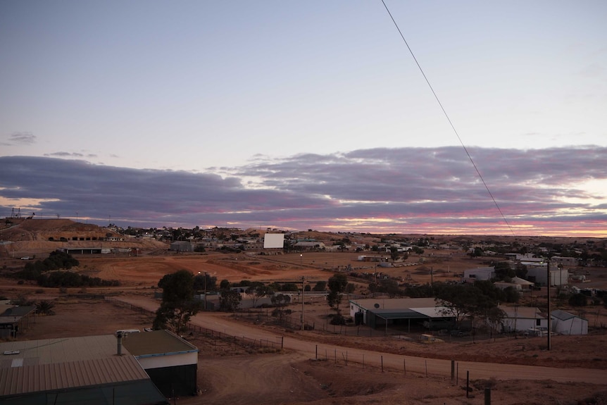 A white screen stands in the middle of a remote township, scattered over small red desert hills