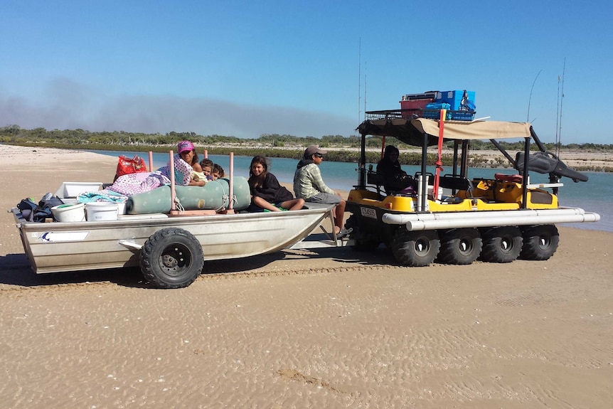 A boat packed up and being towed to the water on a beach.