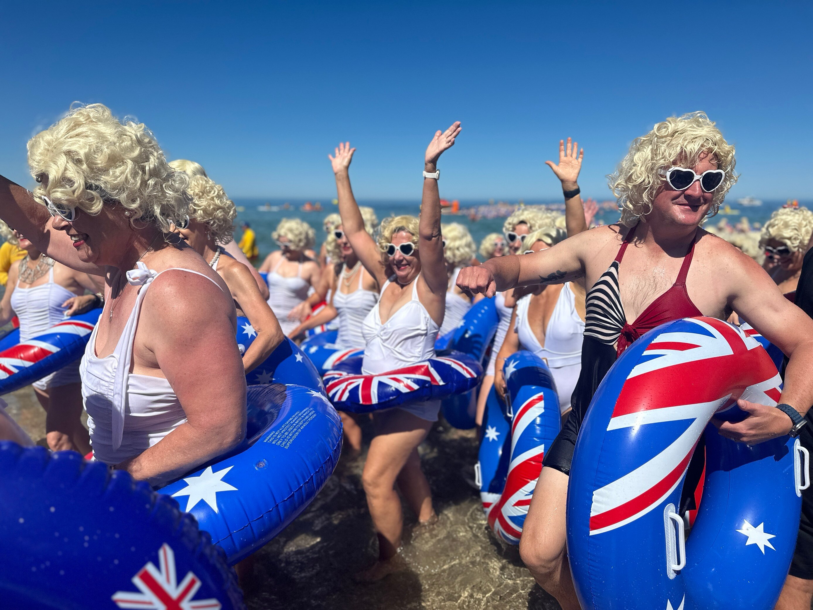 Swimmers with blue floaties and blonde wigs in the ocean.