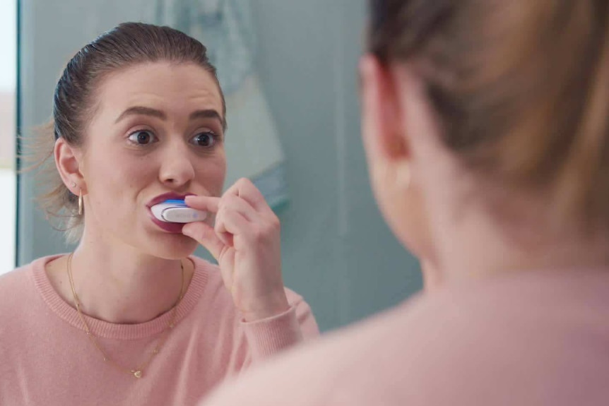 A woman looks in the mirror while using a teeth-whitening mouthguard.