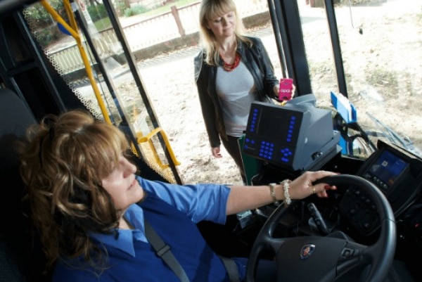 A passenger gets on a bus while the bus driver sits at the wheel