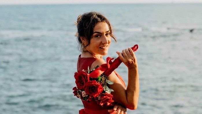 A woman by the sea wearing a red dress and holding a bouquet of flowers