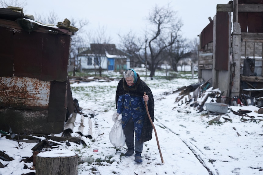 A woman walks in the snow holding onto a walking stick. 