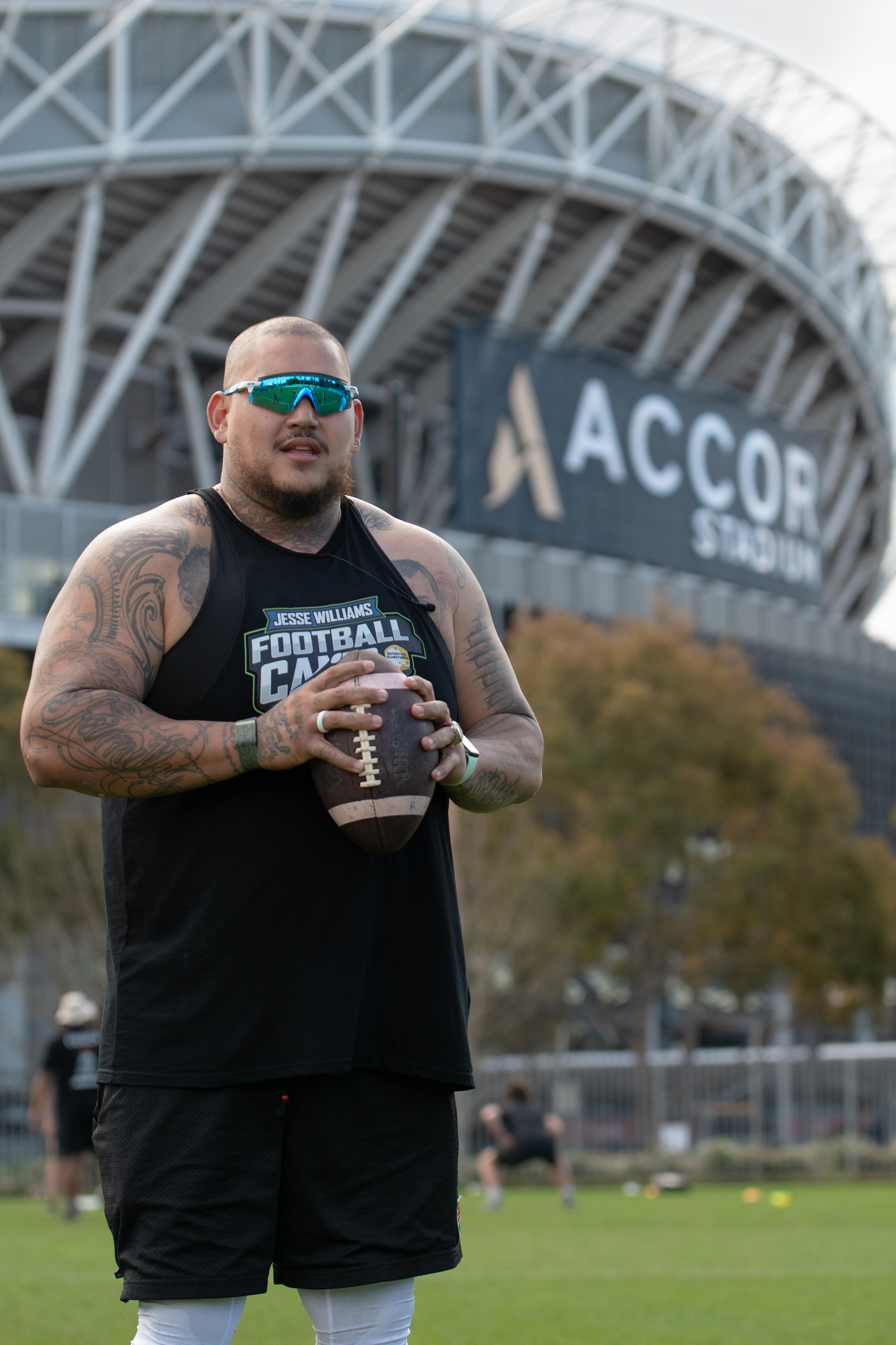 Jesse Williams holds an American football standing outside Stadium Australia.