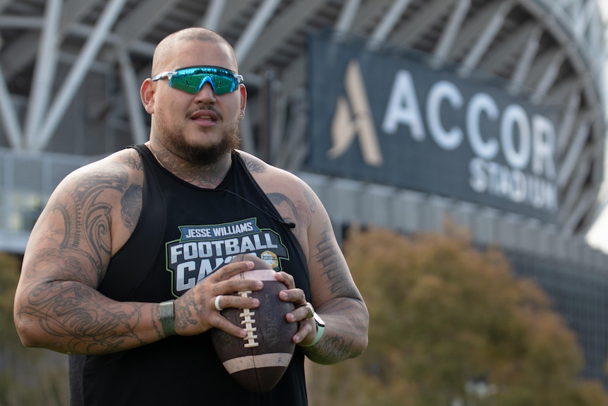 Jesse Williams holds an American football standing outside Stadium Australia.