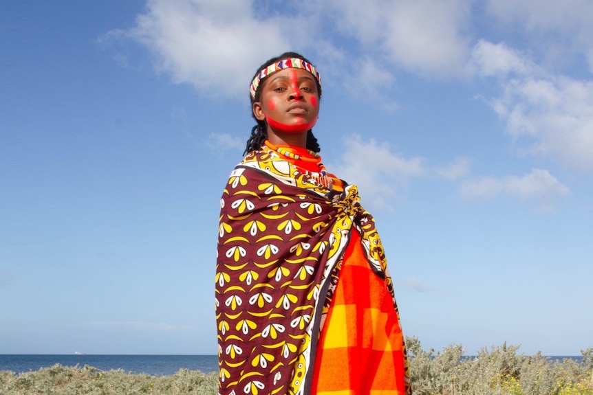 A 2022 press shot of Elsy Wameyo dressed in traditional Kenyan clothes against a blue sky background